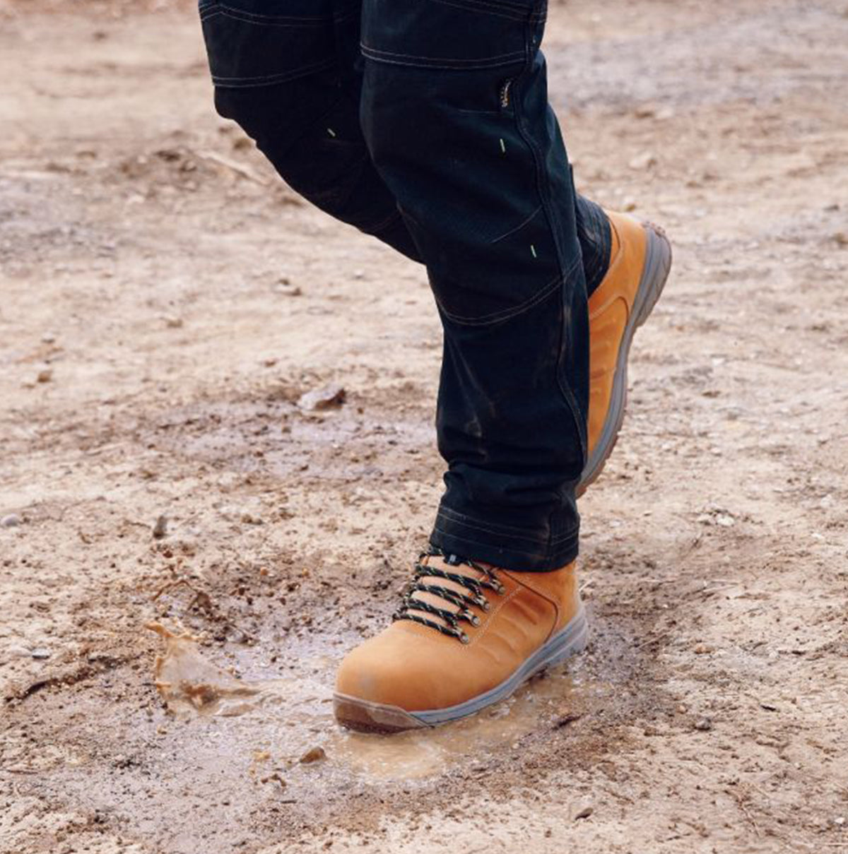 Apache MOOSE Unisex Boots Wheat side view on muddy ground, showcasing lace-up design and ankle height.