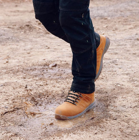 Apache MOOSE Unisex Boots Wheat side view on muddy ground, showcasing lace-up design and ankle height.